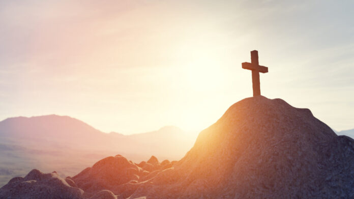 Imagem do por do soul e uma cruz em cima de uma montanha